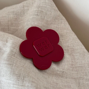 Macro shot of dark red acetate flower hair clip with wer wer engraving on linen background