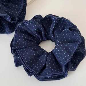 Detail of navy blue polka dot fabric scrunchie with ruffled edges and soft texture
