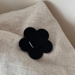 Close-up of a black acetate flower hair clip with engraved lettering on linen fabric
