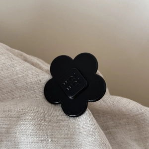 Detailed macro view of glossy black acetate flower hair clip with embossed lettering