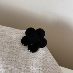 Close-up of black acetate flower hair clip with shiny finish and brand engraving