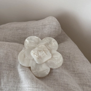 Macro detail of white acetate flower hair clip featuring engraved wer letter logo