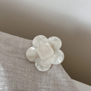 Detailed close-up of cream white acetate flower hair clip with pearl luster and engraving