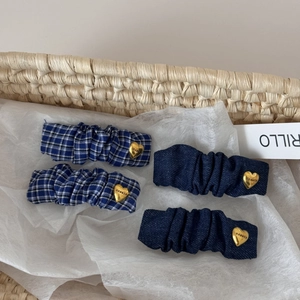 Close-up of four pleated blue fabric hair clips with gold heart buckles in a woven basket