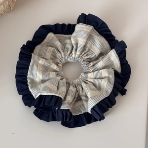 Detail of a large scrunchie with navy blue ruffled edges and black striped inner fabric