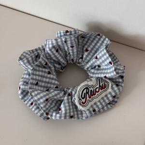 Dettaglio di uno scrunchie a scacchi blu con cuori rossi e logo ricamato