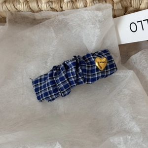 Close-up of blue pleated fabric hair clip with a gold heart pendant and engraving