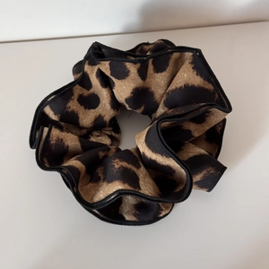 Detail showing high-elastic leopard print scrunchie with satin texture and black stitching