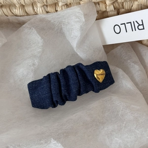 Macro shot of blue denim pleated hair clip featuring a gold heart buckle with engraving