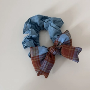 Détail d'un chouchou en tissu bleu clair avec nœud à carreaux marron et bleu sur blanc