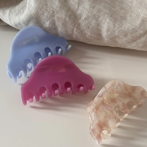Trois pinces à cheveux demi-lunes en acétate bleu, violet et marbré sur un tissu blanc