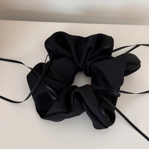 Détail du chouchou noir à nœud ruban avec texture de tissu plissé et rubans élégants longs