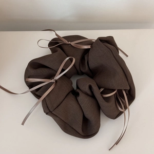Gros plan sur un chouchou marron foncé avec texture sergé et petits nœuds en ruban