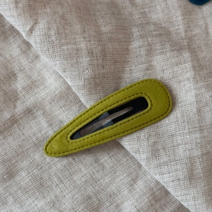 Detail of olive green velvet hair clip with visible stitching on beige linen background