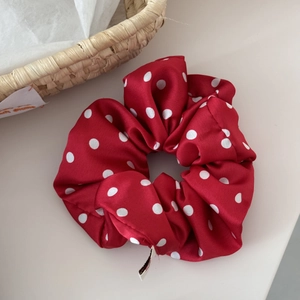 Detail of red polka dot satin scrunchie with soft pleated texture and elegant white tag