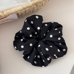 Detailed shot of black polka dot satin scrunchie with soft pleats on white surface
