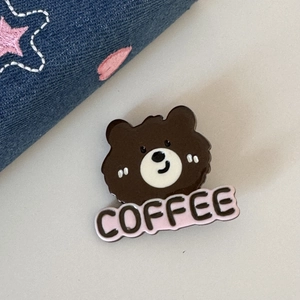 Vue détaillée d'une broche ours marron avec lettrage COFFEE rose sur un tissu en denim