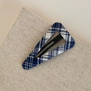 Detail of blue and white checkered fabric covering a triangular metal hair clip on linen