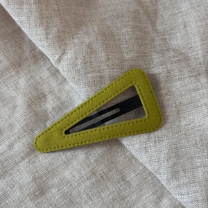 Detail of lime green velvet triangle hair clip with neat stitching on beige linen