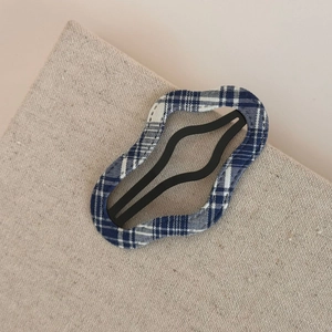 Detailed view of wave-shaped blue and white plaid fabric hair clip with black matte metal