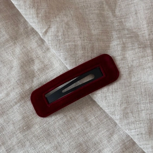 Detail of dark red velvet BB hair clip with fine stitching on a linen background