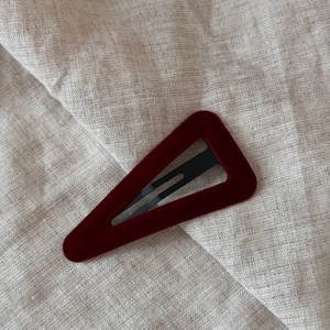 Detail of dark red velvet triangular hair clip with hollow center on beige fabric