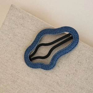 Detail of blue denim plaid hair clip showing white stitching and matte black metal base