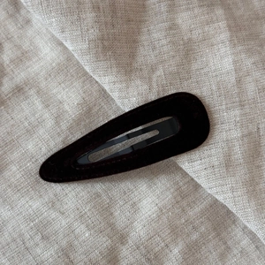 Macro shot of dark velvet teardrop hair clip on textured linen fabric background