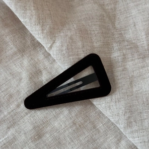 Detailed view of black velvet triangle snap hair clip on a textured linen background