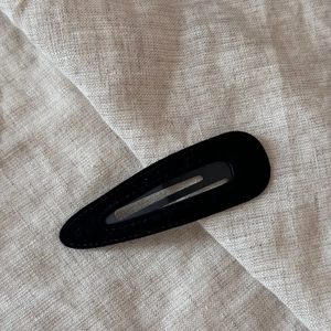 Detail view of black velvet waterdrop BB hair clip on beige linen background