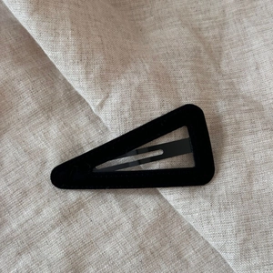 Close-up of a black triangular velvet hair clip on a minimalist beige linen background