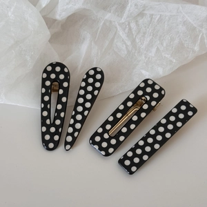 Close-up of four-piece black and white polka dot hair clips with golden metal base