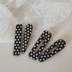 Detail of four-piece black and white polka dot hair clips with golden metal duckbill grips