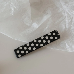Close-up of a rectangular hair clip with black and white polka dot pattern on white texture