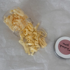Élastiques à cheveux plats jaunes sortant d'un pot transparent avec autocollant merci