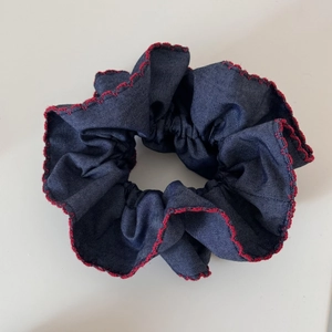 Detailed close-up of blue denim scrunchie with vibrant red scalloped embroidery