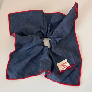 Detail of navy denim scrunchie with red scalloped edges and a fabric brand label