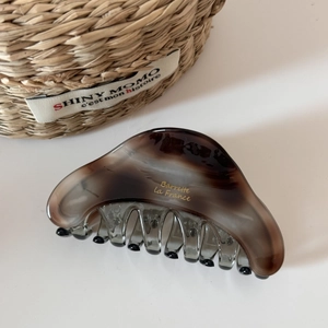 Detail of large acetate hair claw clip featuring dark amber marble pattern and gold text