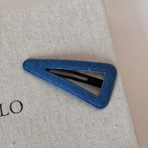 Detailed close-up of a blue denim triangle hair clip on a beige textured fabric background