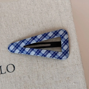 Detailed close-up of blue and white plaid fabric wrapped triangle snap hair clip on linen