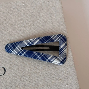 Close-up of blue plaid fabric triangle hair clip on textured beige linen background