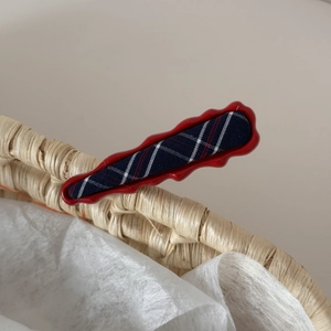 Detail of red wavy hair clip with navy plaid fabric on a light woven basket background