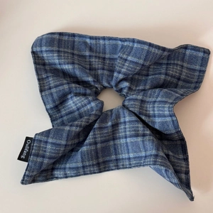 Detailed view of blue plaid fabric scrunchie with a woven brand label and textured finish