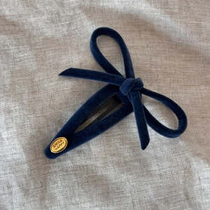 Detailed view of dark blue velvet bow hair clip with engraved golden smile happy label