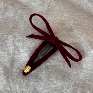 Detail of burgundy velvet bow hair clip with a gold-tone oval metal smile charm