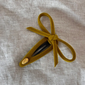 Detailed macro of mustard yellow velvet bow hair clip with gold Smile Happy metal tag