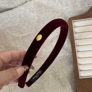 Close-up of a burgundy velvet headband with a gold-tone oval plaque and elegant logo detail