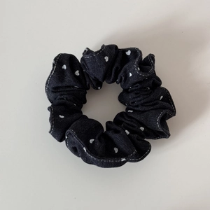 Detailed close-up of dark denim hair scrunchie with white heart patterns and fine stitching