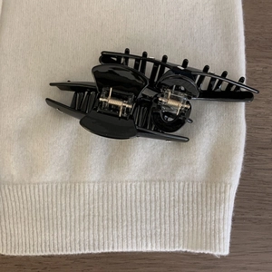 Detail of two large black glossy acetate shark hair claws with gold springs on white fabric