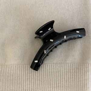 Detail of a large black acetate hair claw clip with rectangular rhinestones on fabric